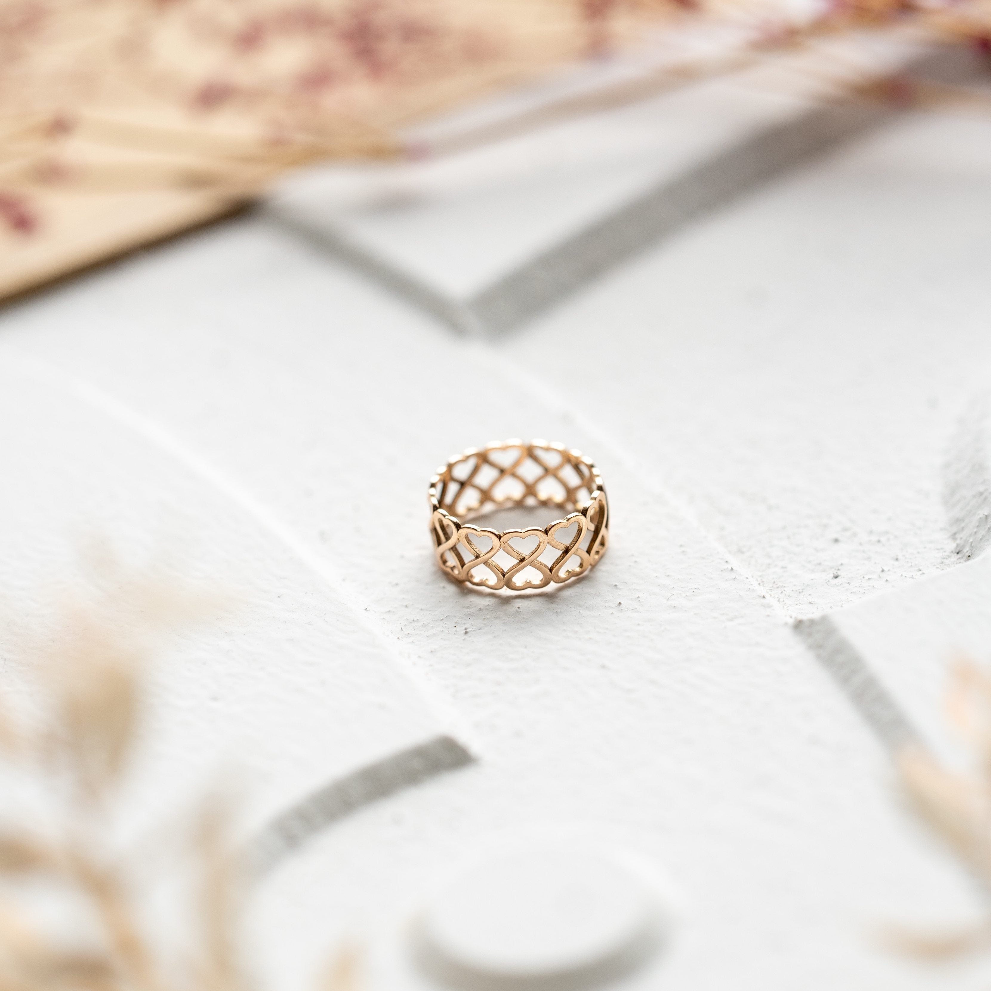 Rose gold heart ring, laying on grey stone surrounded by lilies.