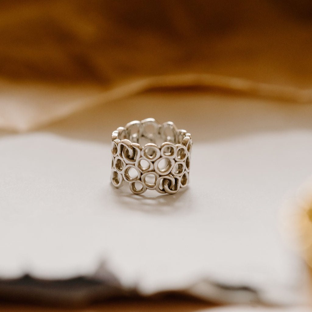 Luxury silver ring on white paper with brown leaves surrounding it. 