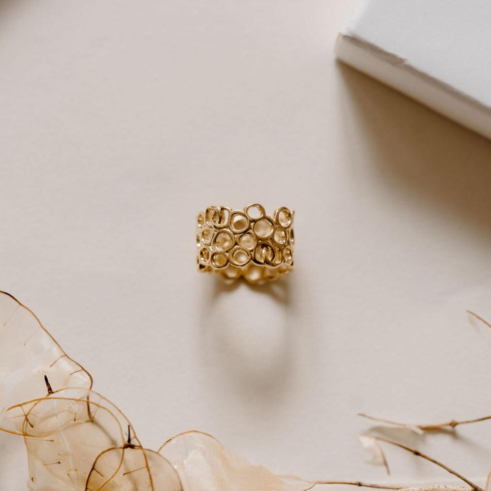 Unique gold ring inspired by inner beauty, on white table with white flowers.